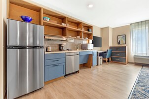 Una cocina moderna con un refrigerador de acero inoxidable, estantes de madera, un microondas y una silla azul.