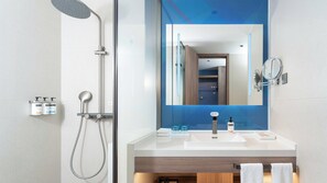 A modern bathroom with a shower, a large mirror, and a sink with toiletries.