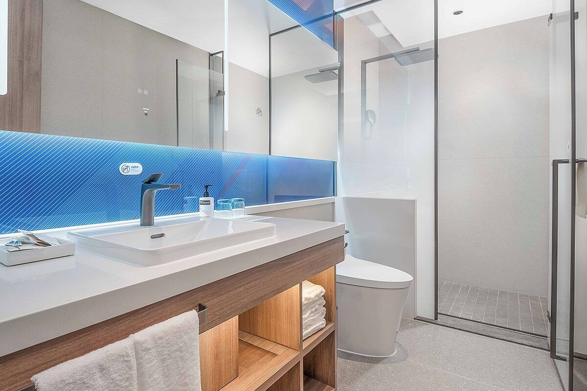 A modern bathroom with a wooden vanity, a glass shower enclosure, and a blue textured wall.