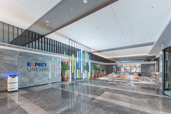A modern lobby with a marble floor, a reception desk, and seating area with orange chairs.