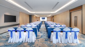A conference room with rows of tables and chairs, a large screen at the front, and a blue carpet. - Holiday Inn Express Foshan Shunde Lecong (Foshan)