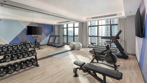 A modern gym with exercise equipment, large windows, and a city view.