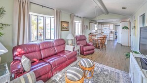 Un salón amplio con un sofá de cuero rojo, una zona de comedor con mesa y sillas de madera, y una cocina al fondo.