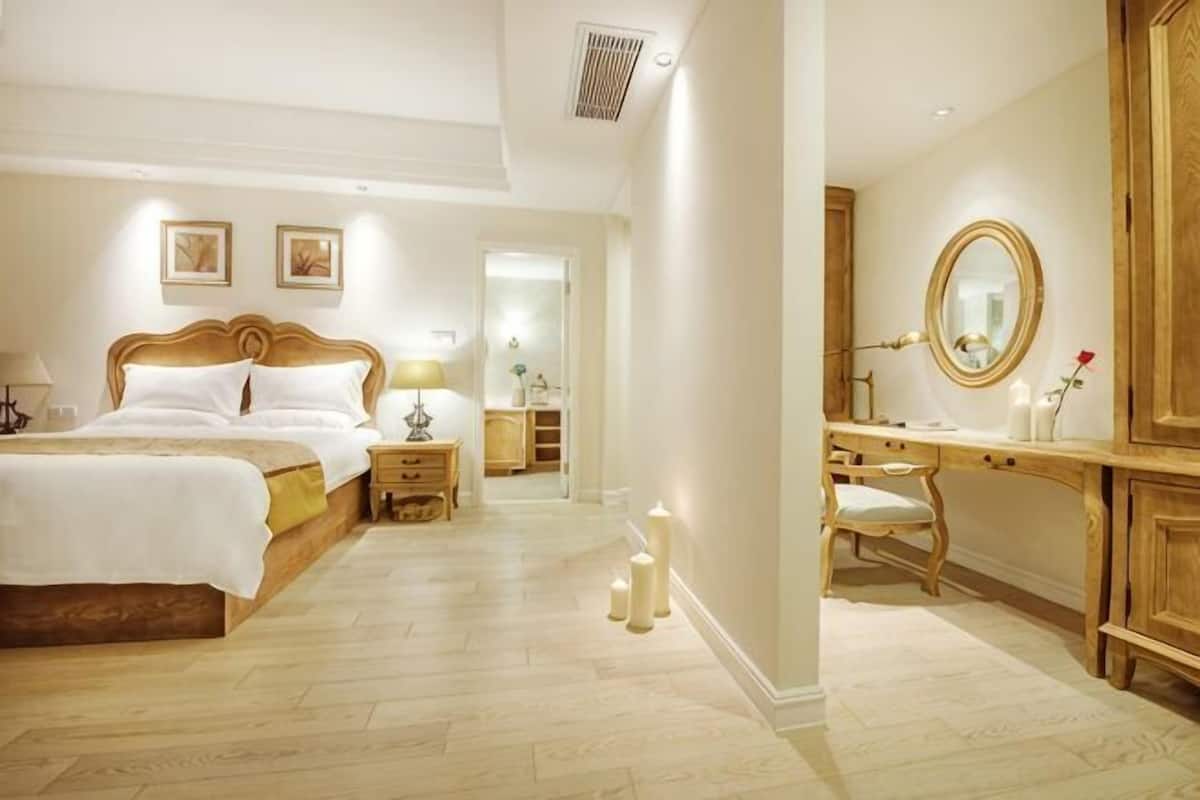A hotel room with a large bed, bedside tables, a vanity with a mirror, and a wooden wardrobe.
