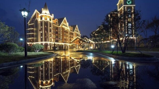 Un hotel imponente con una torre de reloj, un estanque reflectante y una fachada bien iluminada.