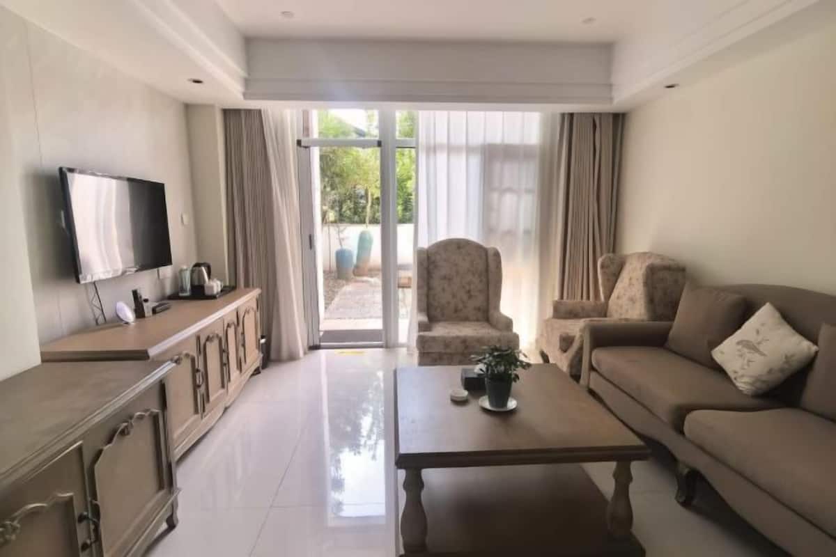 A living room with a sofa, armchair, coffee table, TV, and a sliding glass door leading to an outdoor area.
