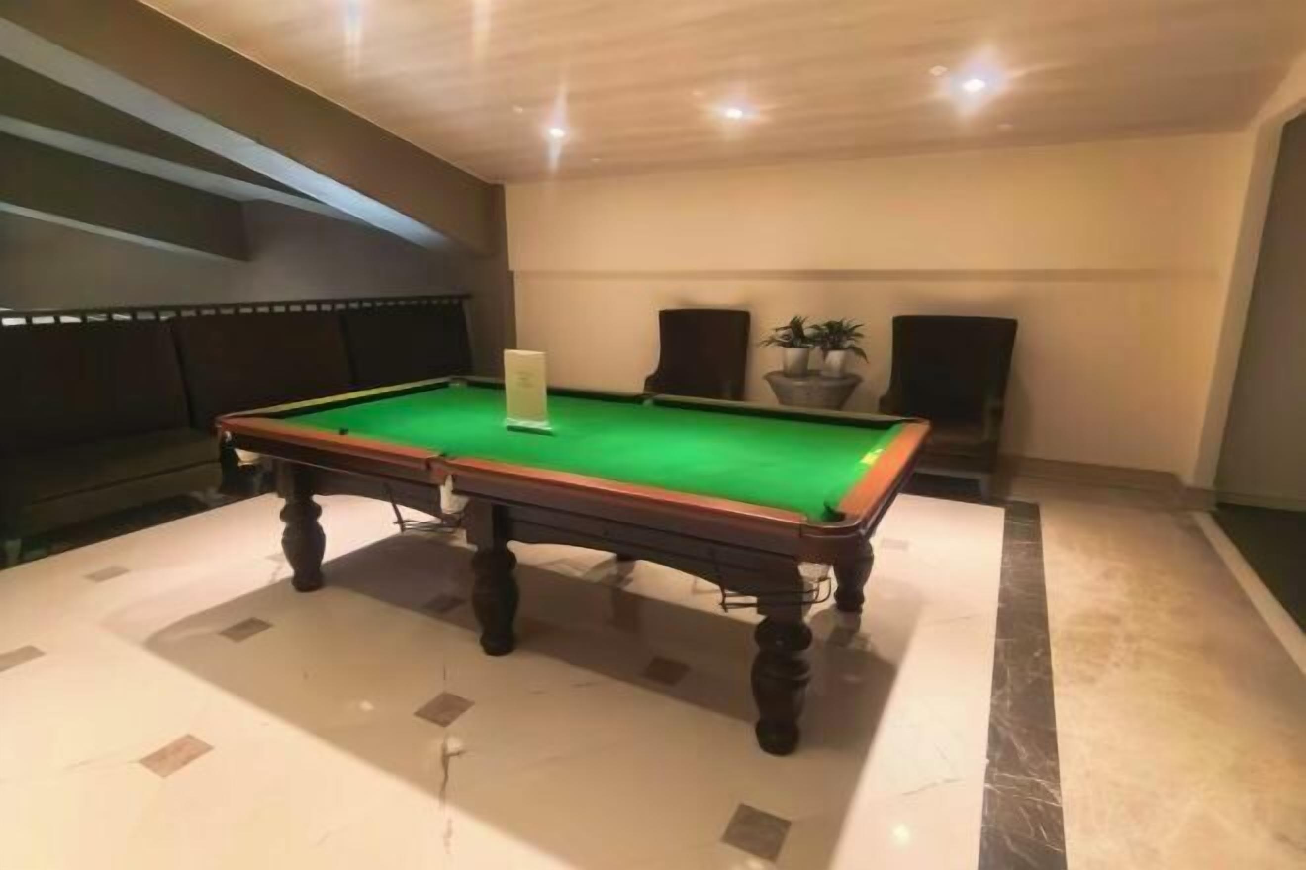A pool table in a room with a marble floor, a potted plant, and a speaker.