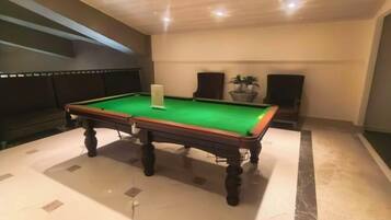 A pool table in a room with a marble floor, a potted plant, and a speaker.