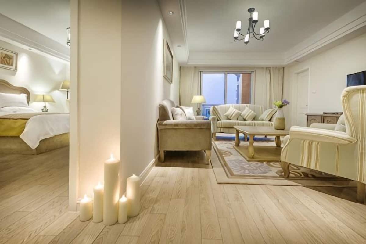 A hotel room with a bed, a sofa, a chair, a coffee table, and a chandelier.