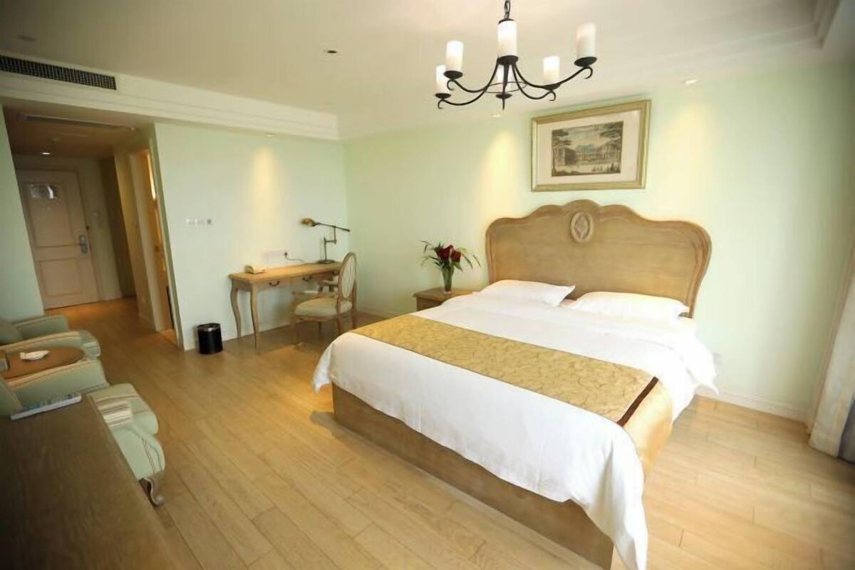 A hotel room with a large bed, a desk, a chair, and a chandelier.