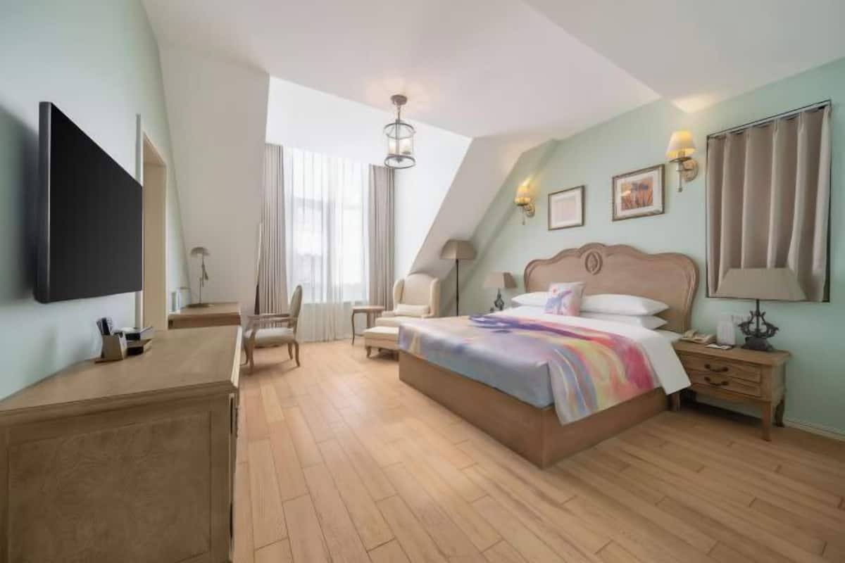 A hotel room with a bed, bedside tables, a desk, a chair, a TV, and a window with curtains.