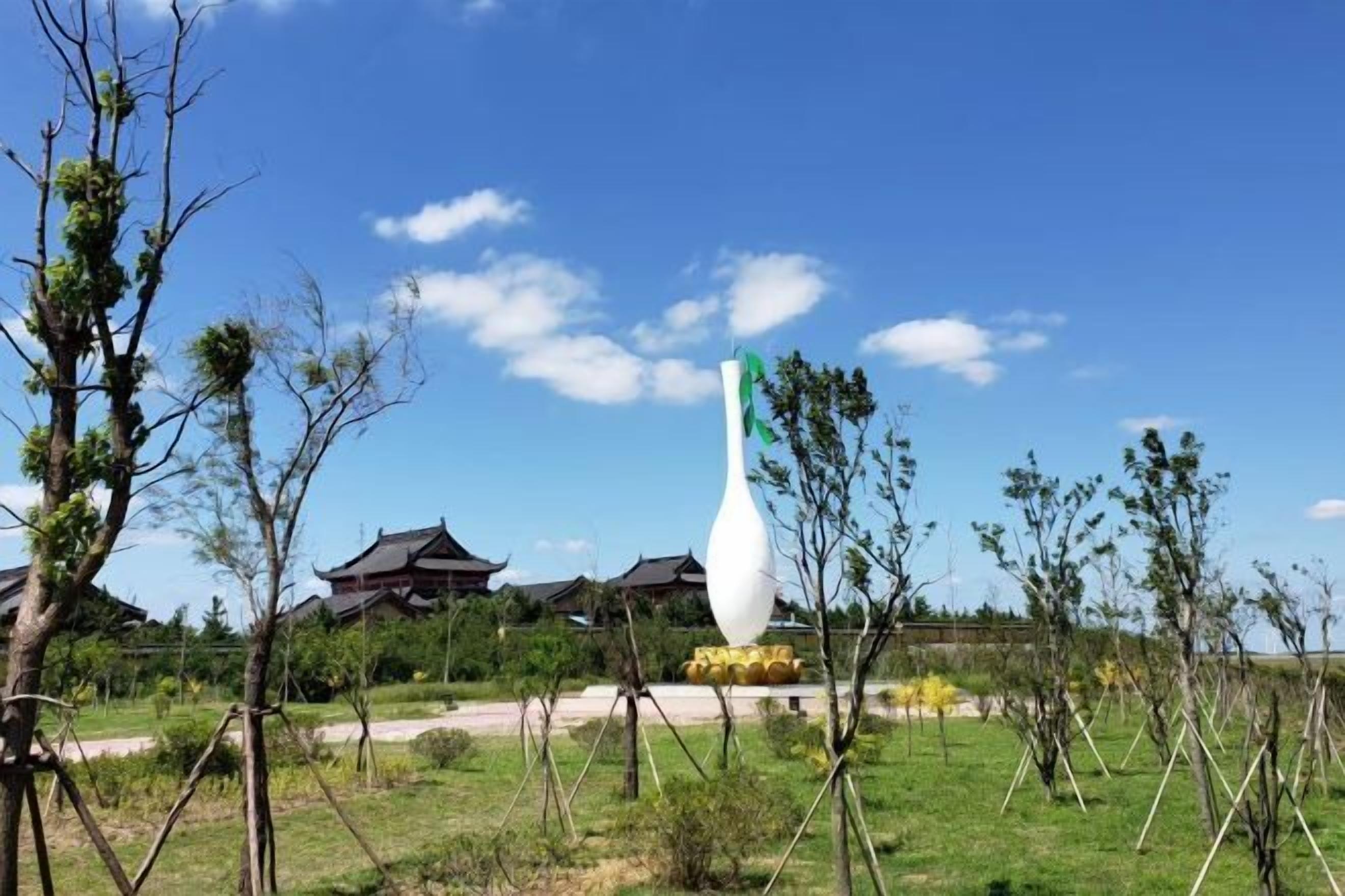 A traditional building with a curved roof, surrounded by a grassy area with young trees and a large white sculpture.