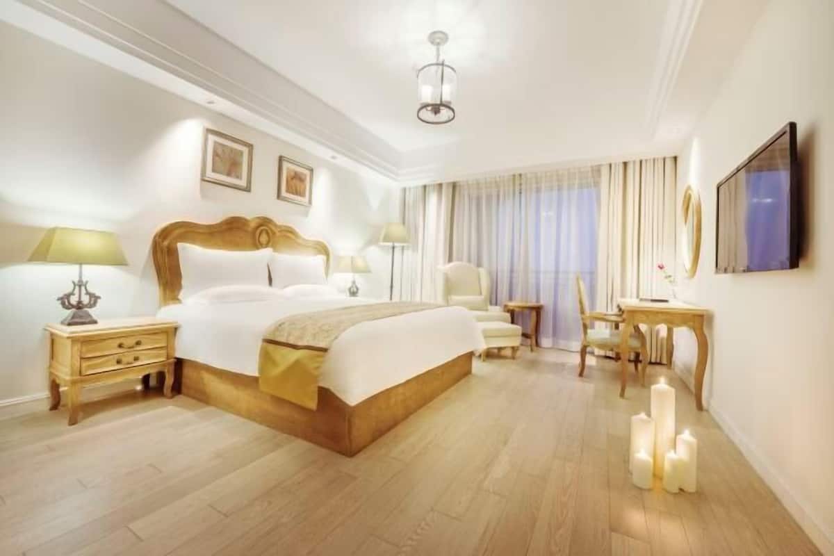 A hotel room with a large bed, bedside tables, a chair, a desk, and a television.