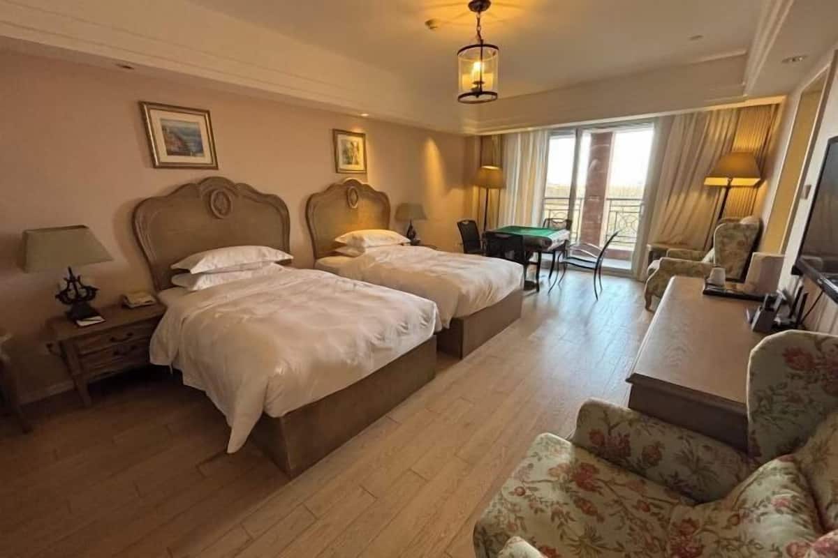 A hotel room with two beds, a desk, a chair, a TV, and a balcony.
