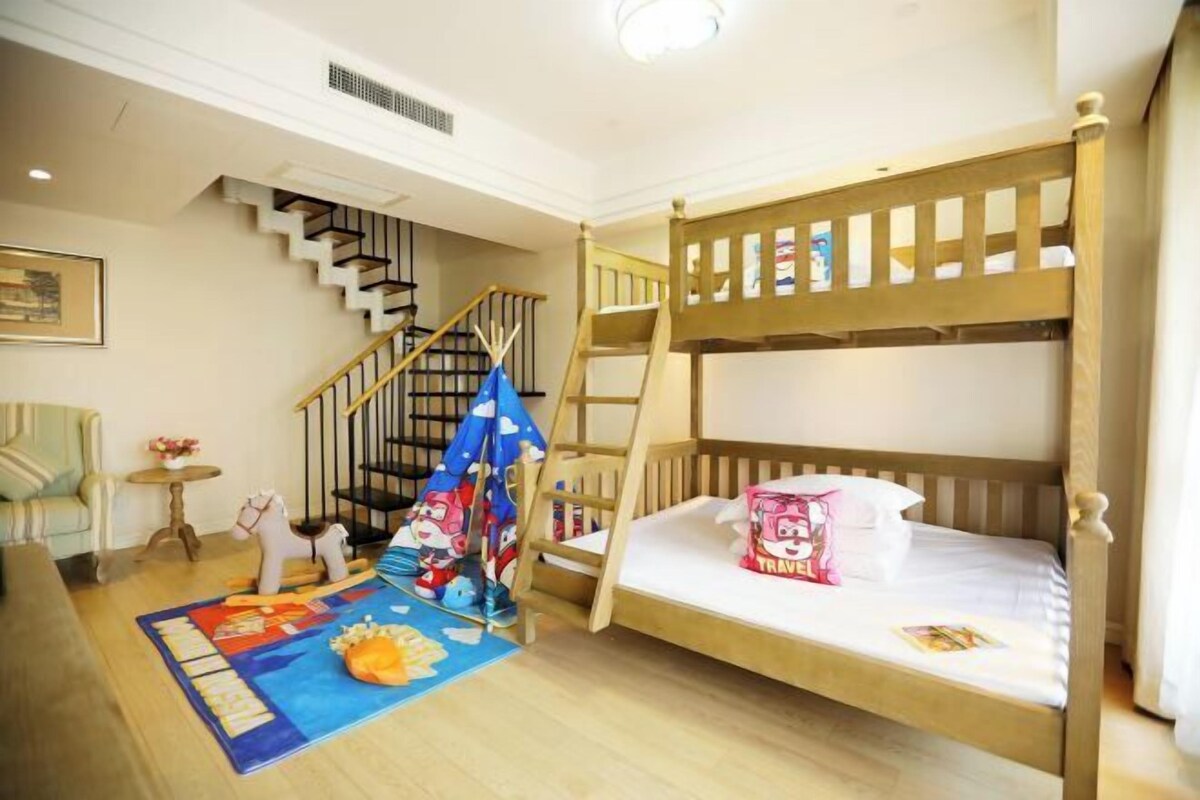 Habitación con literas, una escalera de madera, una mesita con un caballo de juguete, un tapete azul con un personaje de caricatura y una escalera.