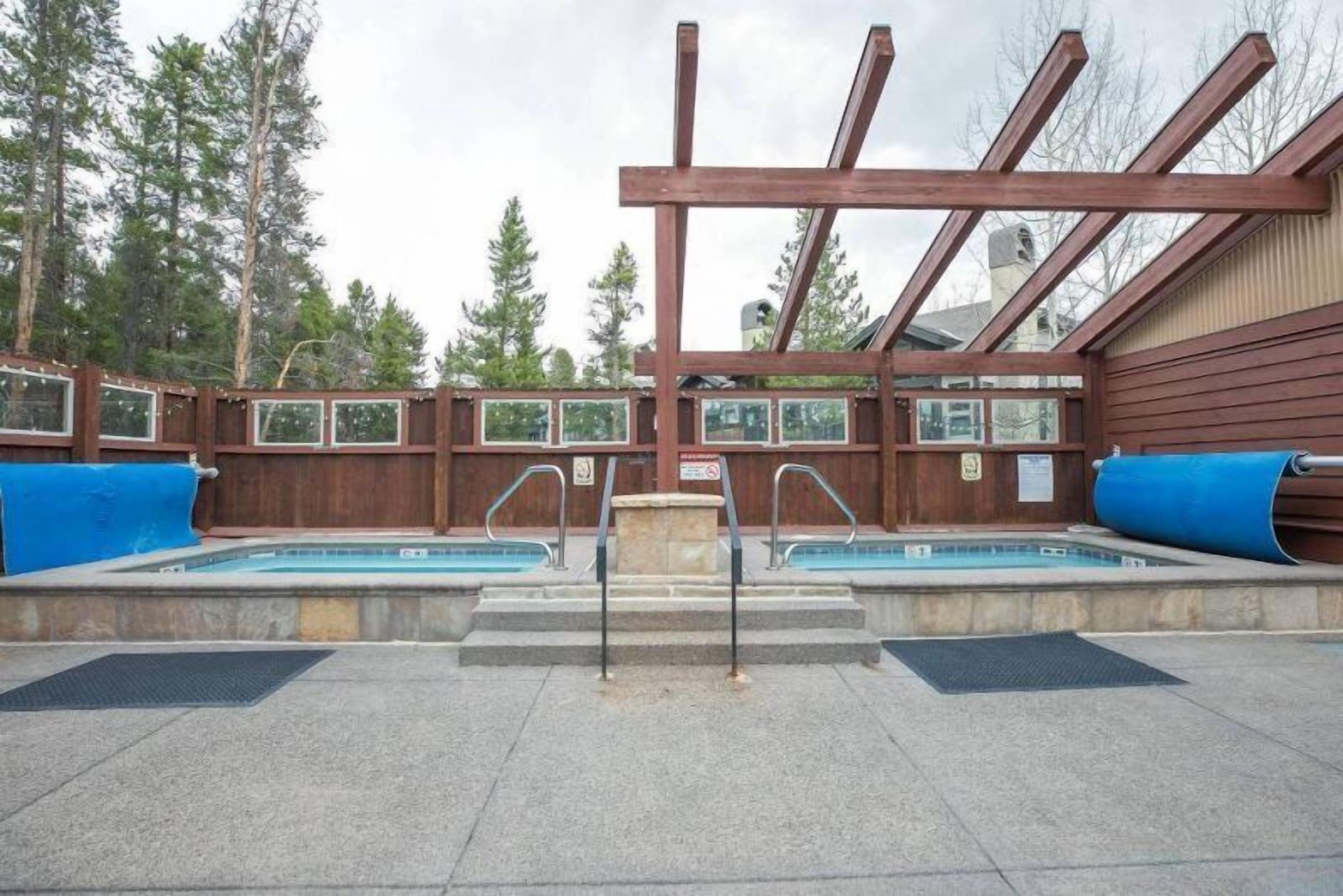 Un área de piscina con dos piscinas, terraza de madera y zona de estar cubierta.
