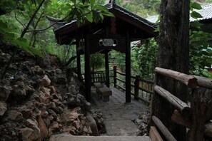 A traditional wooden structure with a tiled roof, surrounded by lush greenery and rocky terrain. - Youtang Cloud Station CourtyardZen-style Inn (Lijiang Shuhe Ancient Town Branch) (Lijiang)