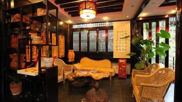 A traditional room with a sofa, wicker chairs, a decorative table, and a bookshelf with various items.