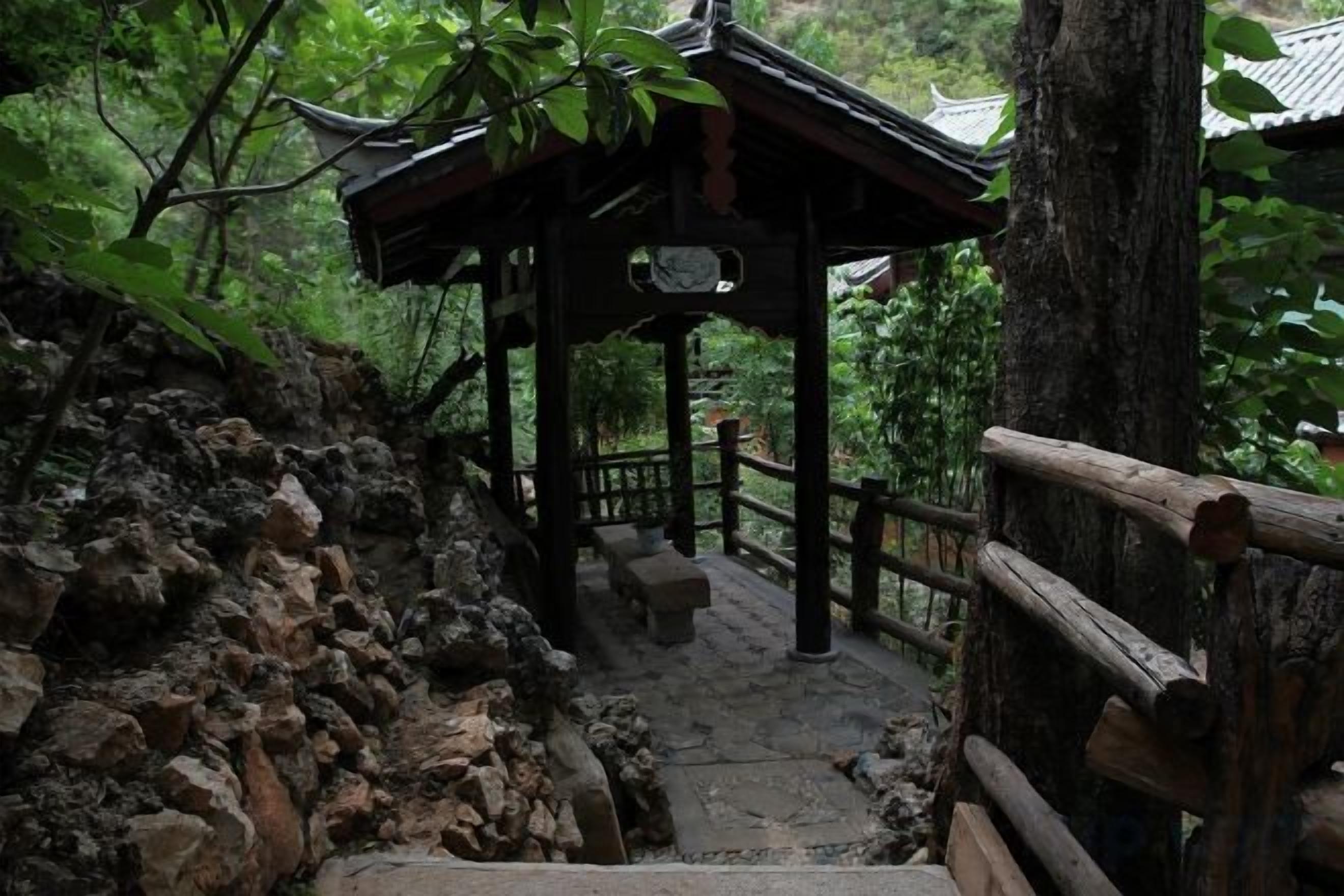 Una estructura de madera con techo, rodeada de árboles y un sendero de piedra.