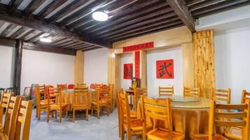Un comedor con varias mesas y sillas de madera, techo alto con vigas a la vista y elementos decorativos rojos en las paredes.