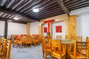 Un comedor con varias mesas y sillas de madera, techo alto con vigas a la vista y elementos decorativos rojos en las paredes.