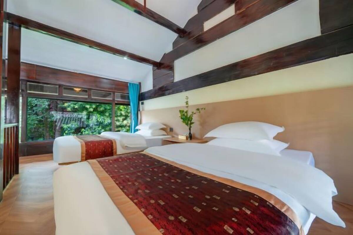 A modern bedroom with a large bed, a small seating area, and a view of greenery through the window.
