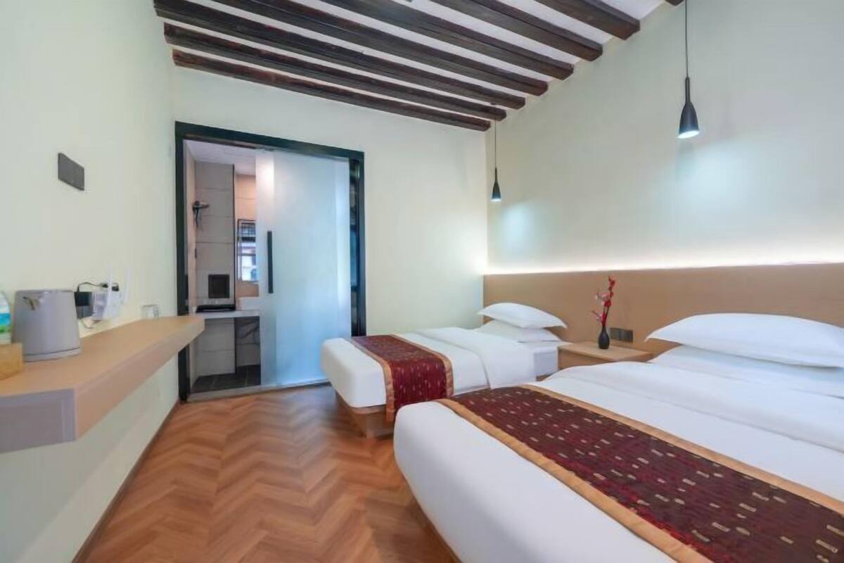 A hotel room with a wooden floor, a large bed with a patterned bedspread, a bedside table with a lamp, and a small desk with a telephone and a cup.