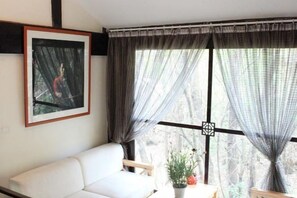 Una habitación con un sofá blanco, un cuadro en la pared y una ventana con cortinas.