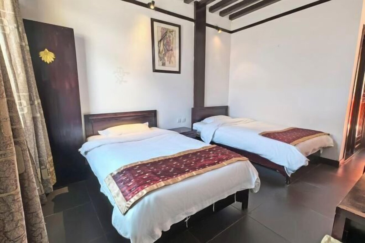 A hotel room with two beds, a dark wooden door, a framed artwork on the wall, and a window with curtains.