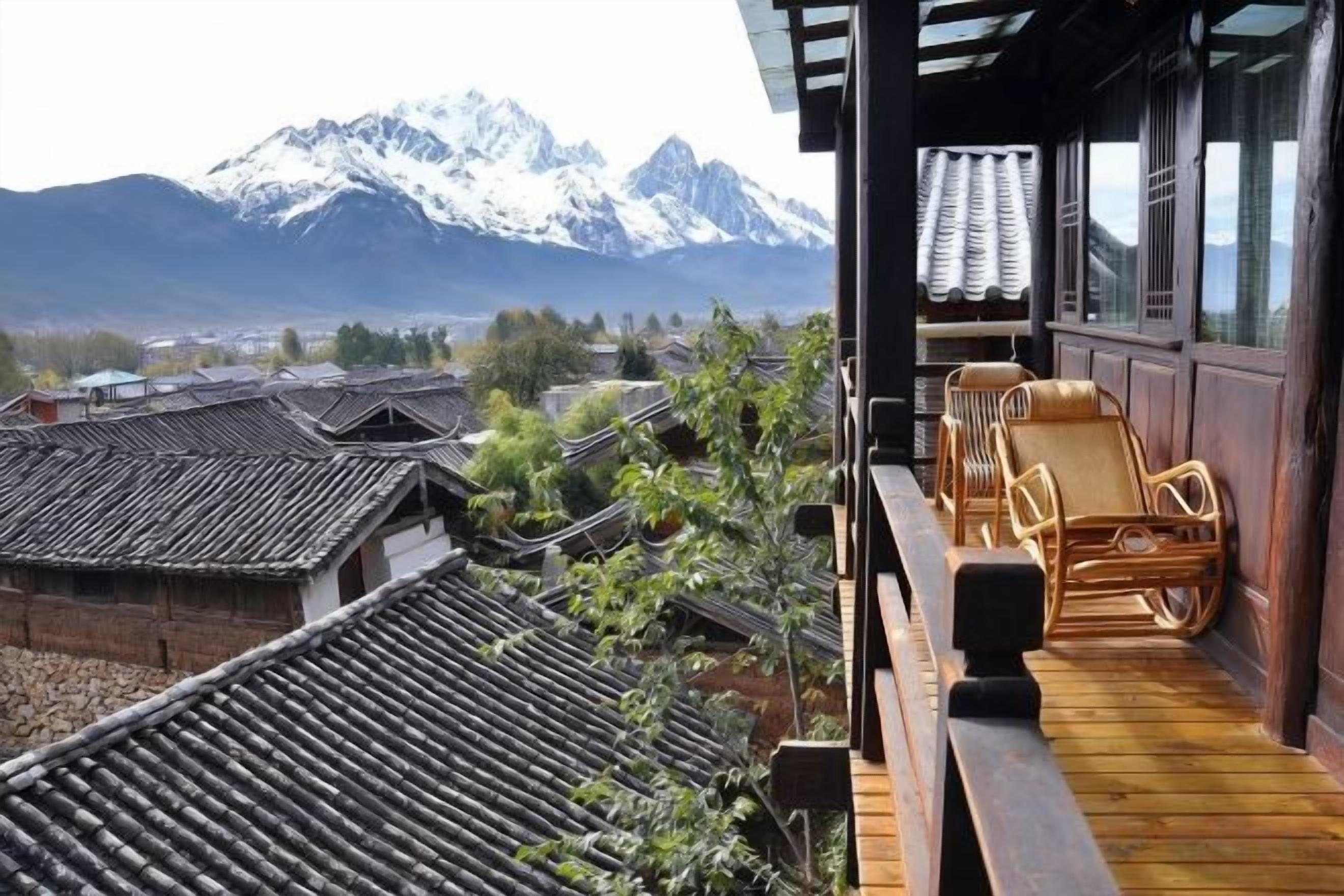 A traditional Japanese-style balcony with tatami flooring and low wooden railings, overlooking a village and snow-capped mountains.