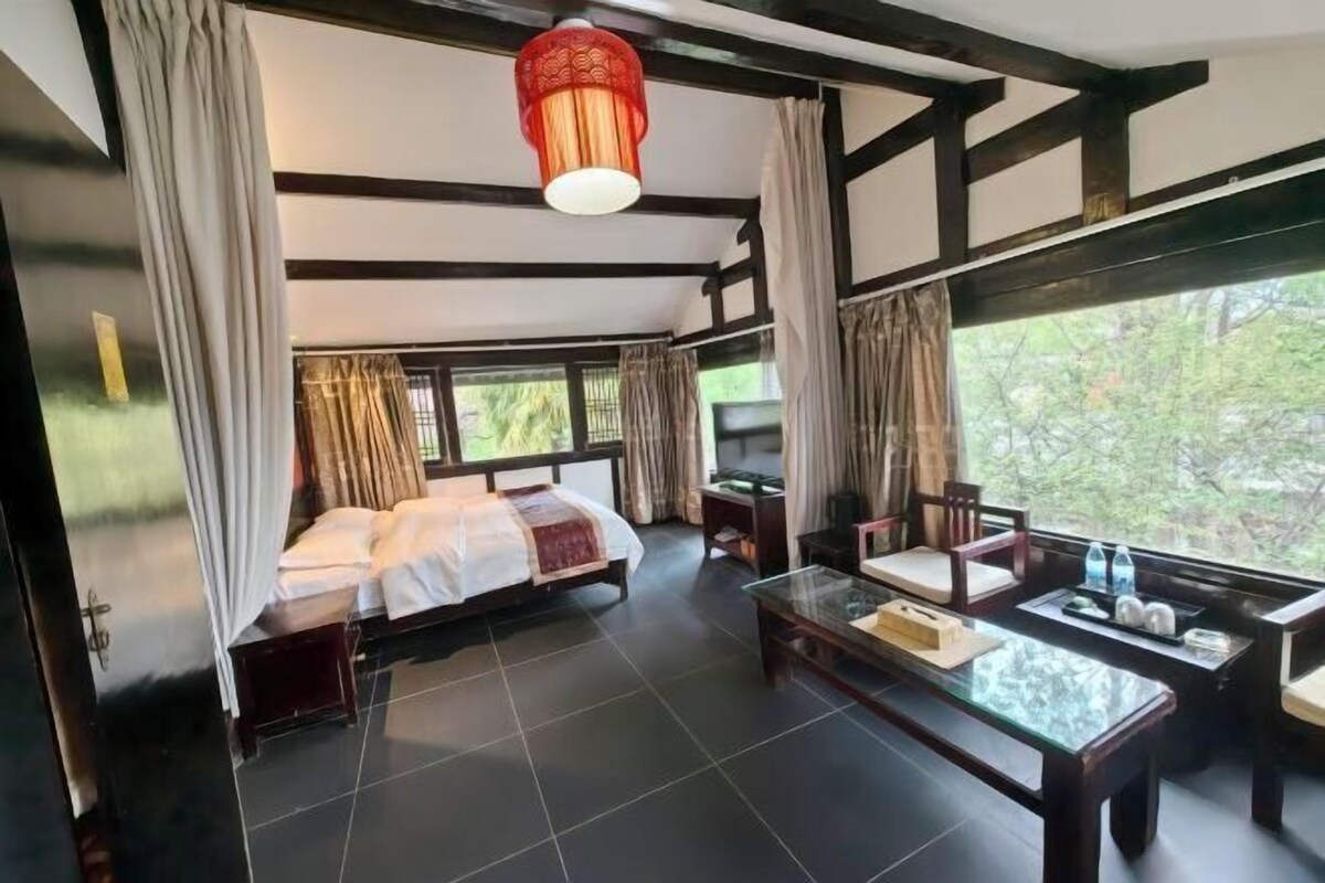 A room with a bed, a glass coffee table, and a view of greenery outside.