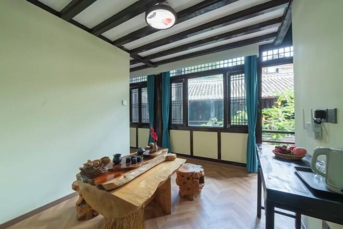 A traditional room with a wooden table, a small stool, and a window with curtains.
