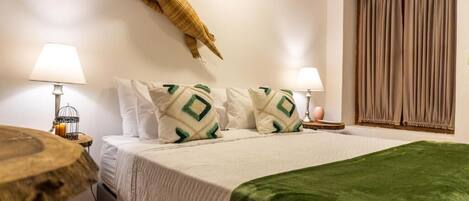 Habitación de hotel con una cama, dos lámparas de noche, un adorno en la pared y una ventana con cortinas.