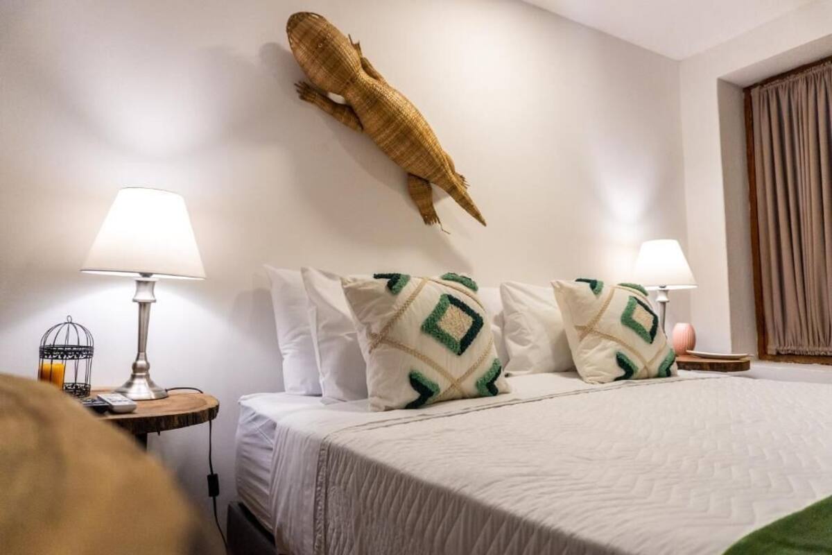 Habitación de hotel con cama, dos mesitas de noche, lámparas, un tapiz decorativo y un ventanal con cortinas.