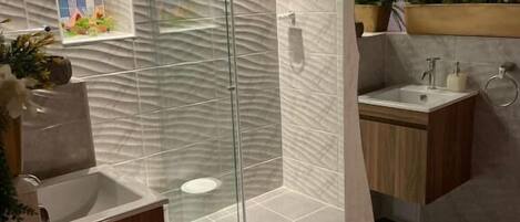 Un baño moderno con cabina de ducha de vidrio, un lavabo y un pequeño tocador.