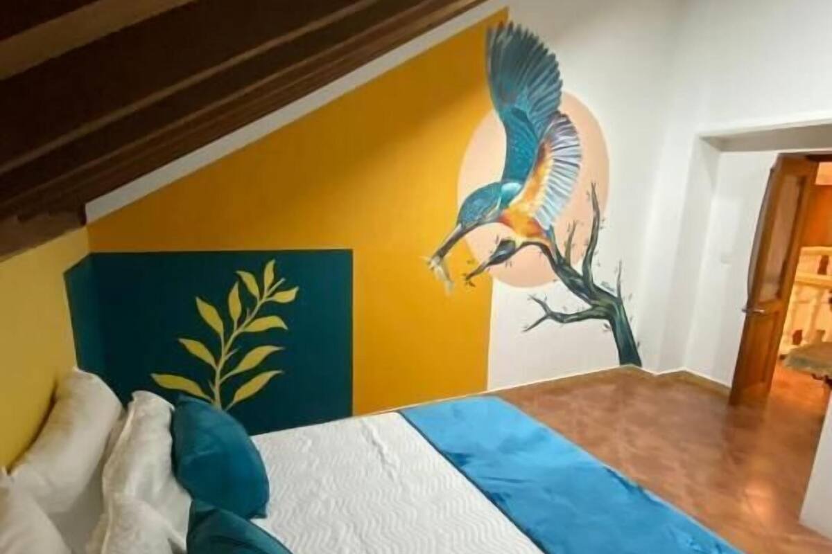 Un dormitorio con cama, almohadas, un mural y una puerta.