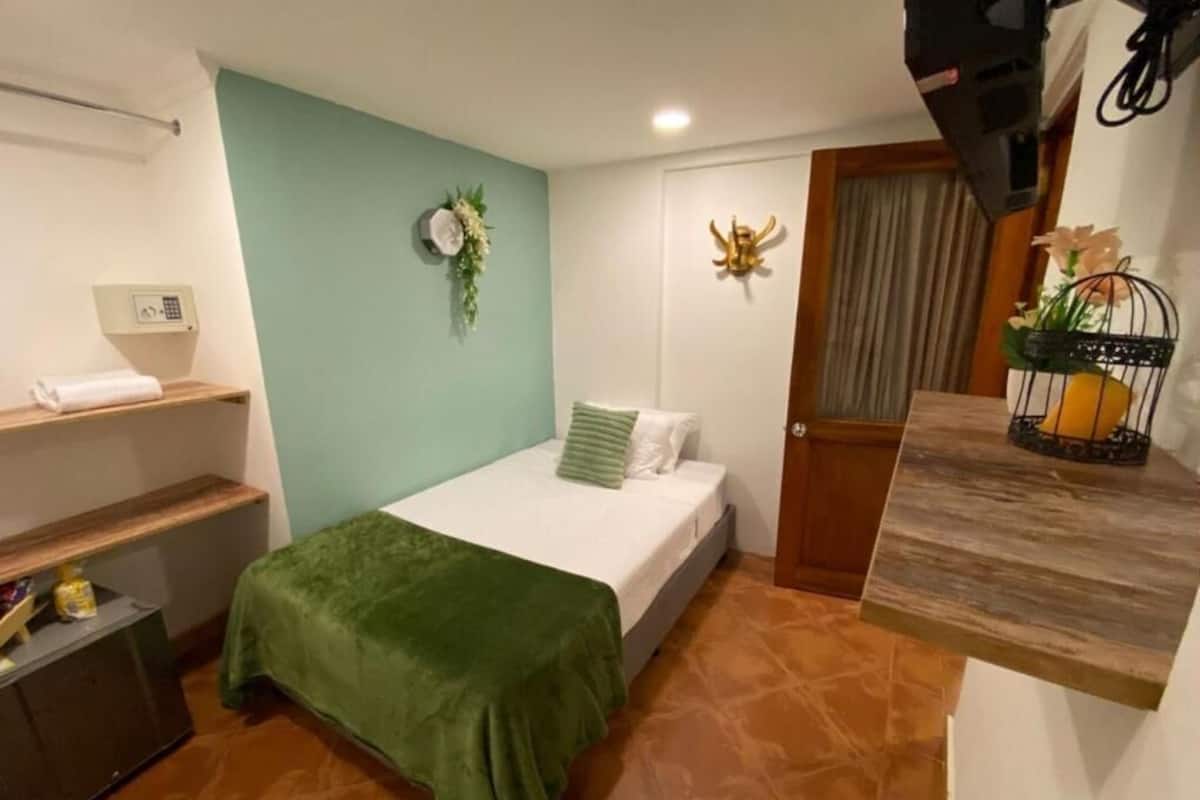 Un dormitorio pequeño y ordenado con una cama, una mesita de noche, un estante y una puerta.