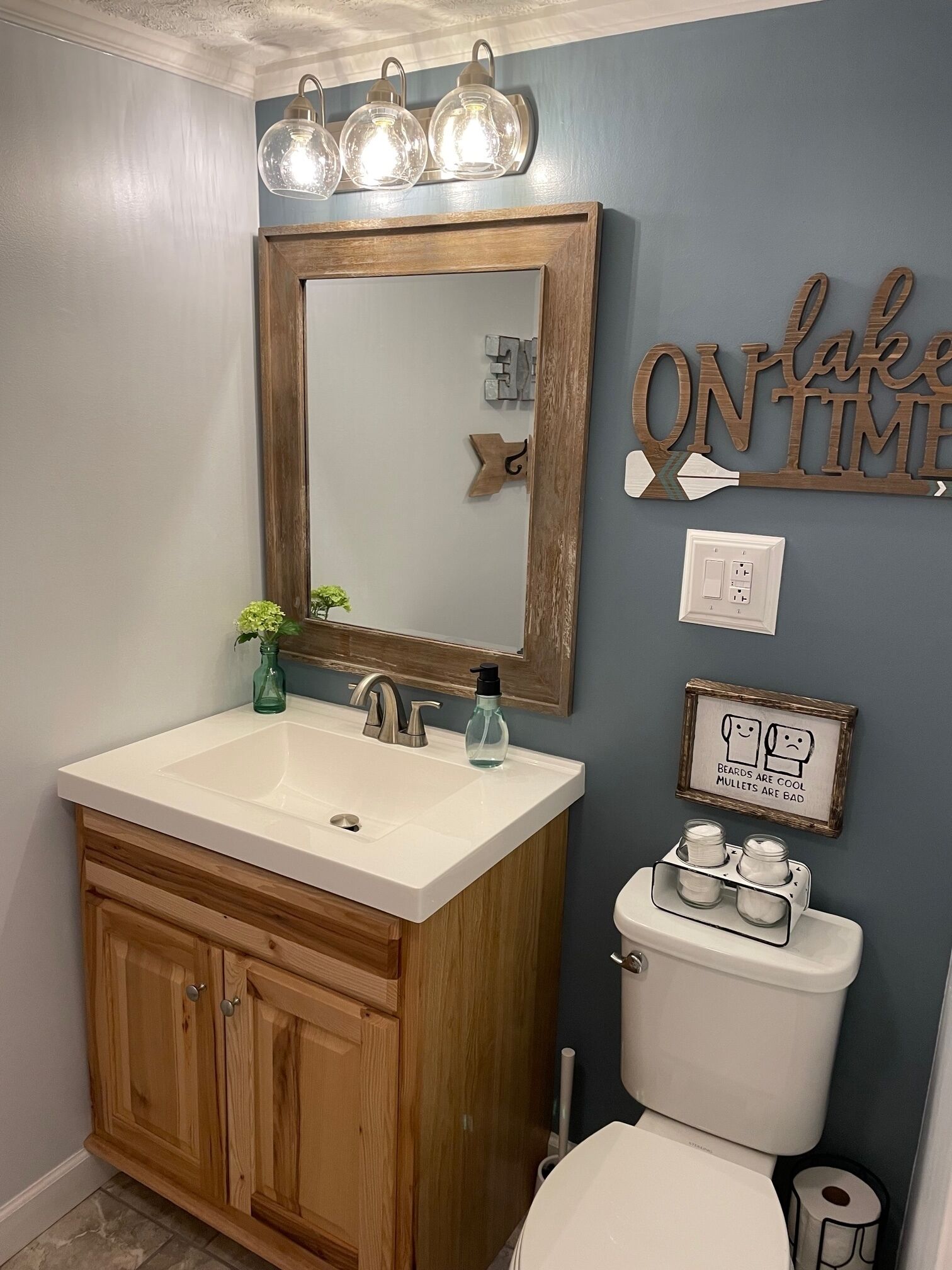 Un baño con tocador de madera, espejo, lavabo, inodoro y decoración en la pared.
