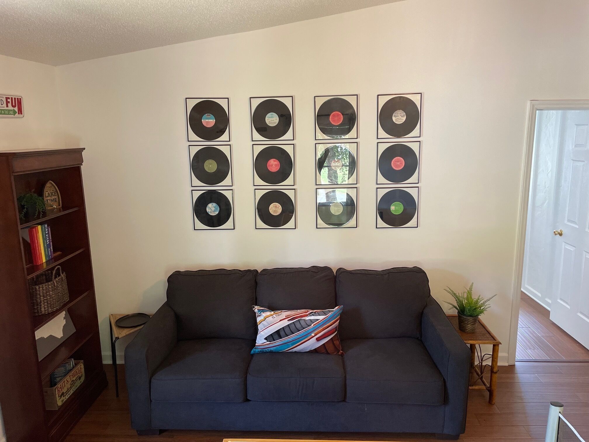 Ein Wohnzimmer mit einem dunkelgrauen Sofa, einem kleinen Beistelltisch mit einer Pflanze und einem Bücherregal mit Büchern und Dekoartikeln.