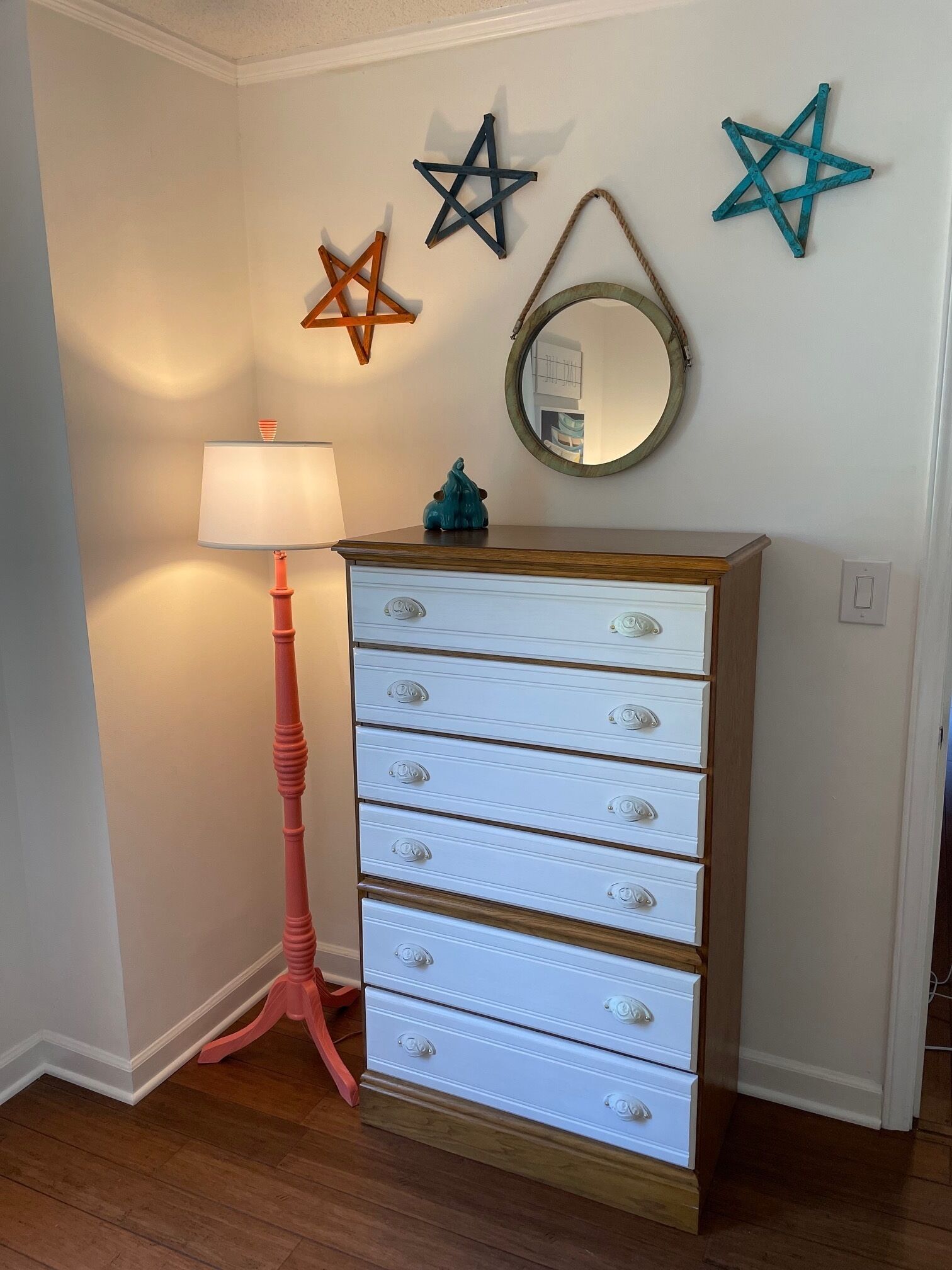 A white dresser with multiple drawers, a pink floor lamp, and three star-shaped decorations on the wall.