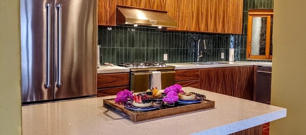 Eine Küche mit Holzschränken, einem Edelstahlkühlschrank, einem Gasherd und einer Holzausziehtischplatte mit einer Schale Essen und Blumen.