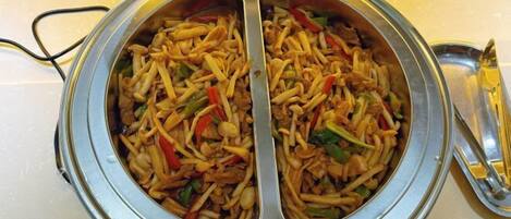 Recipiente metálico redondo com uma colher, cheio de um prato de macarrão com legumes.