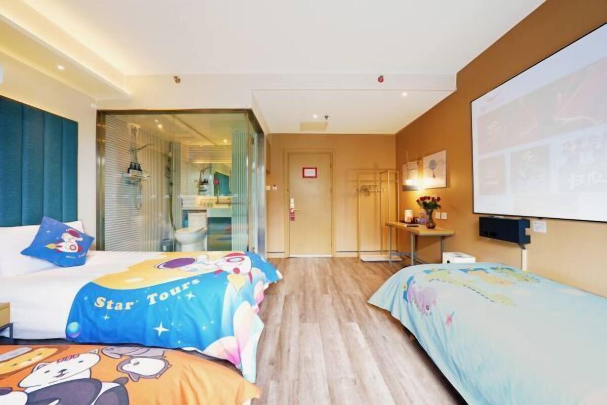 A hotel room with two beds, a TV, a desk, and a bathroom visible through a glass door.