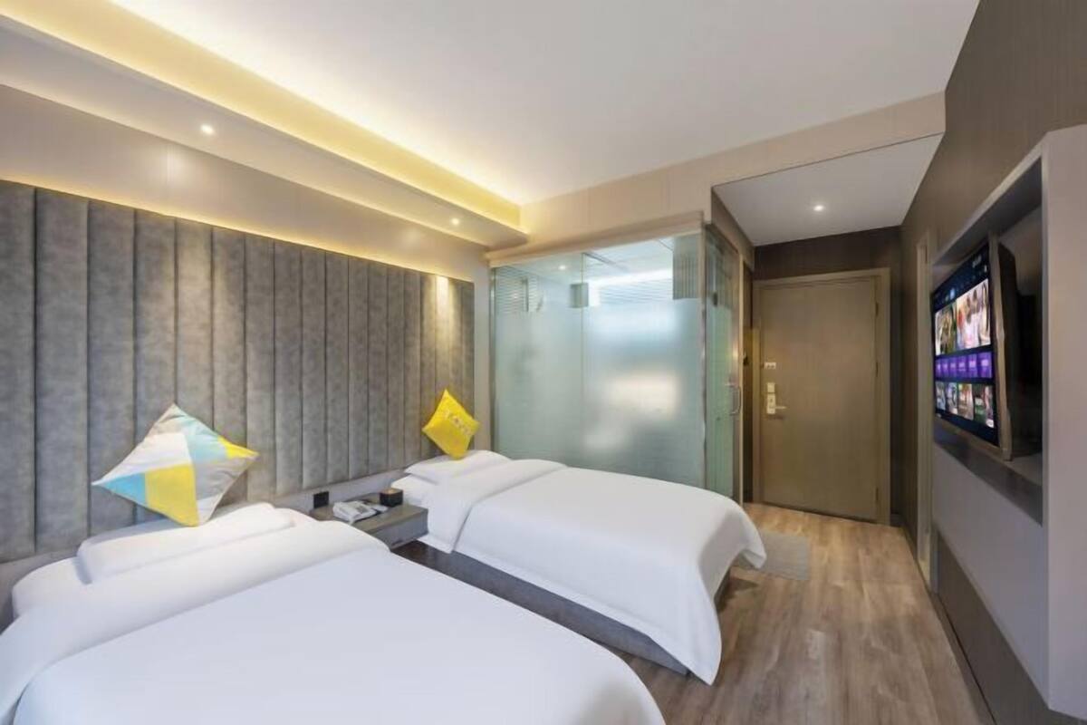A hotel room with two beds, a glass partition, a television, and a wooden floor.