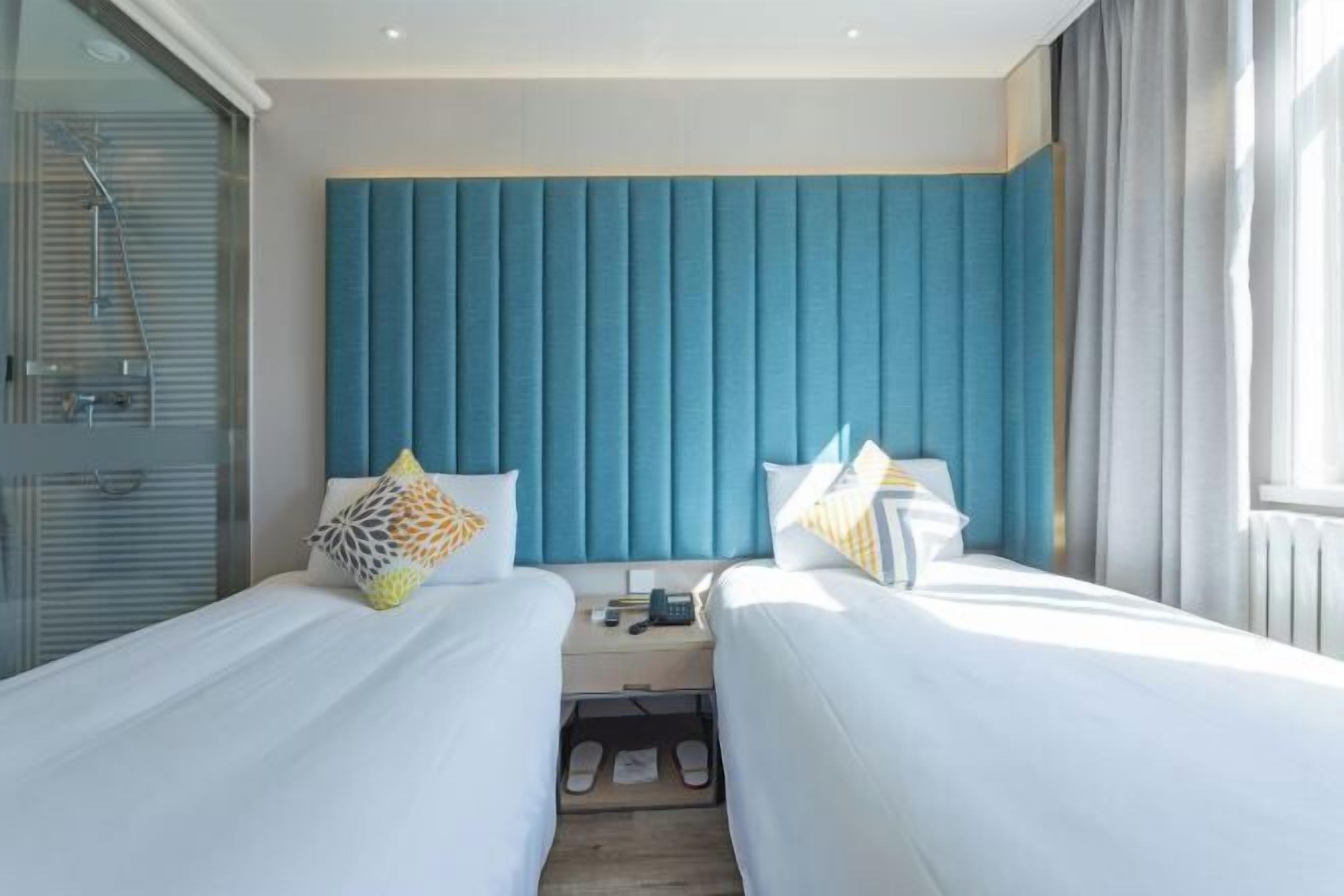 Una habitación de hotel con dos camas, un cabecero azul y una cabina de ducha de vidrio.