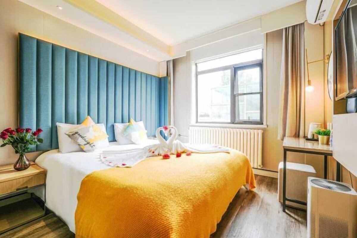 A hotel room with a bed, a desk, a radiator, and a window.