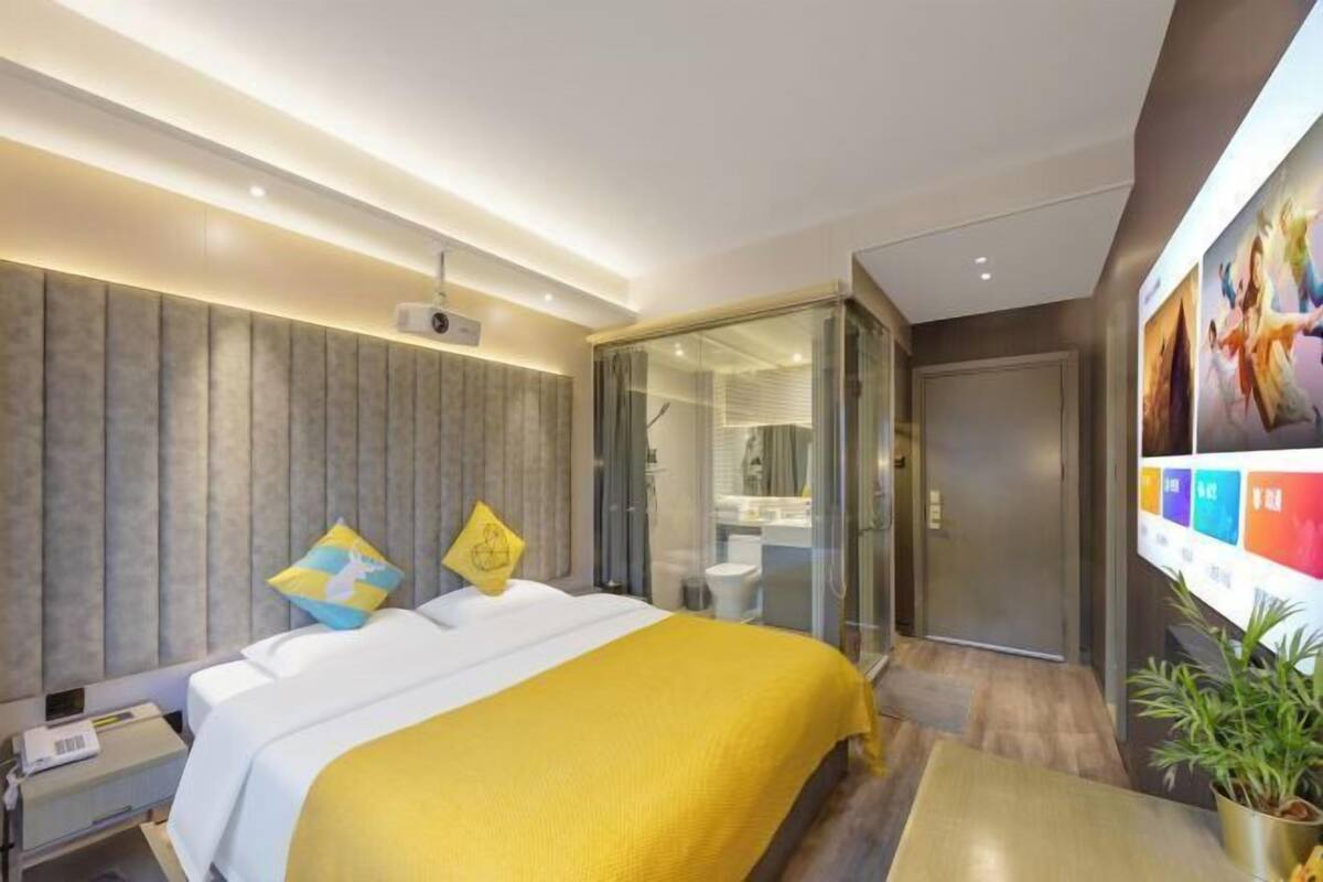 A modern hotel room with a large bed, a glass shower enclosure, and a wall-mounted TV.