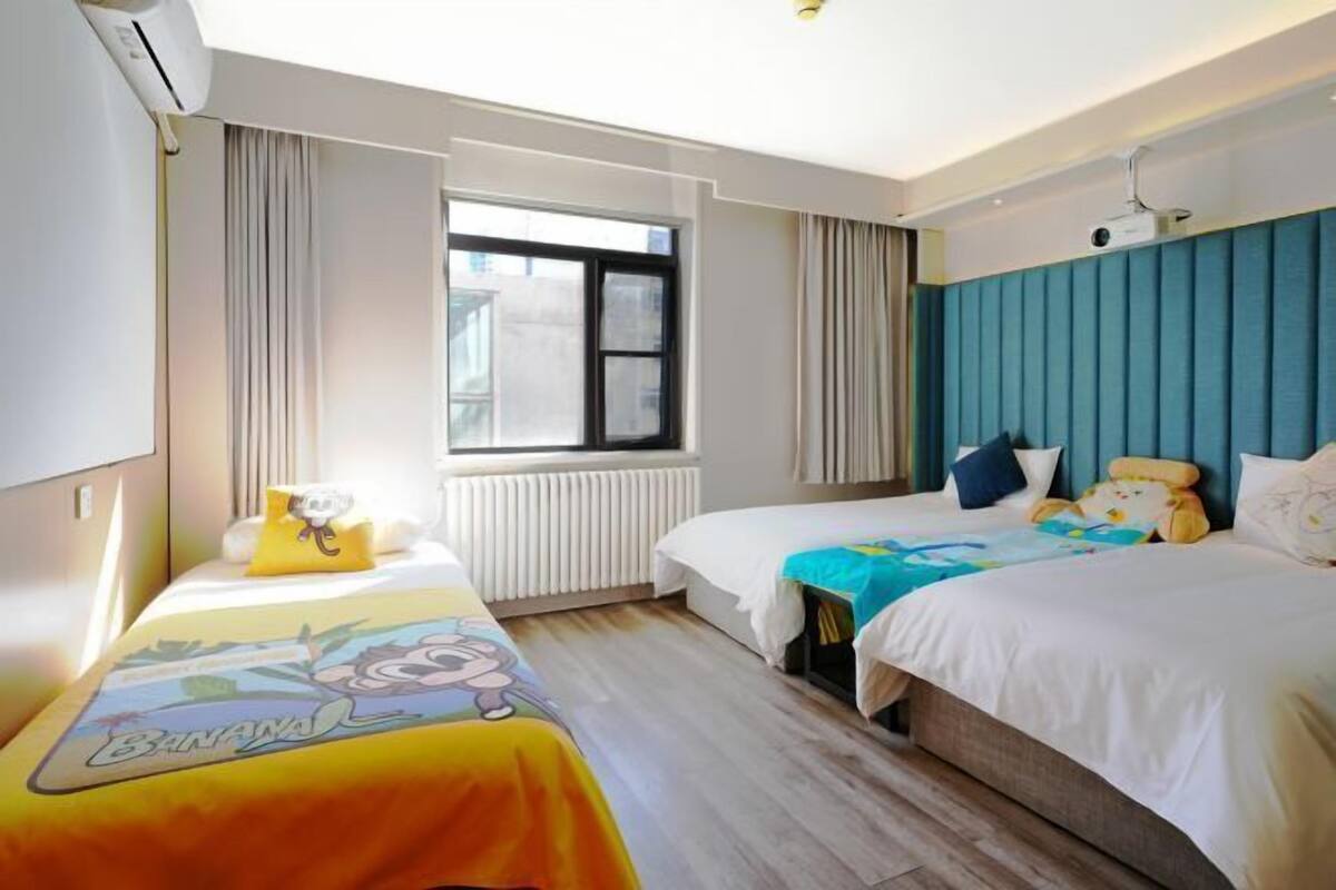 A hotel room with two beds, a window, a radiator, and a ceiling projector.