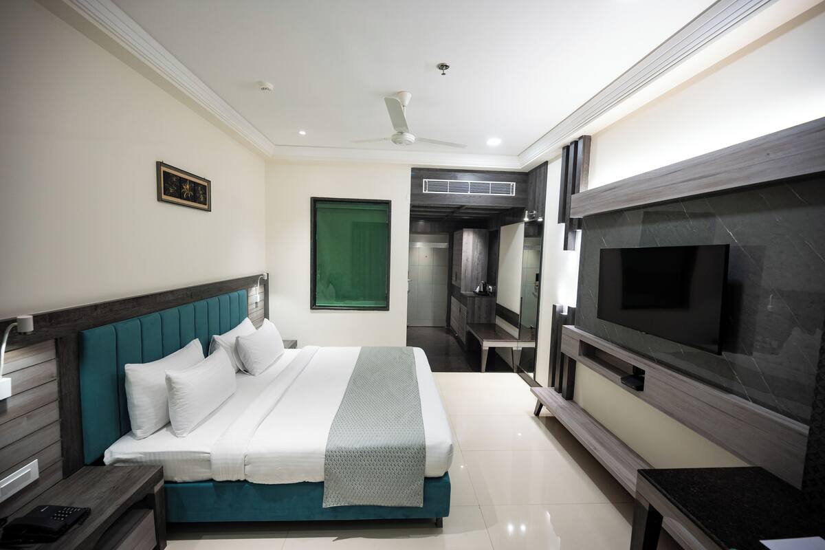 A modern bedroom with a large bed, a TV, and a bathroom visible through an open door.