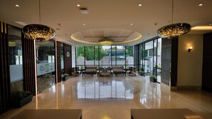 A spacious lobby with a polished floor, modern furniture, and large windows offering a view of the outside. - The Hotel Mudra (Varanasi)